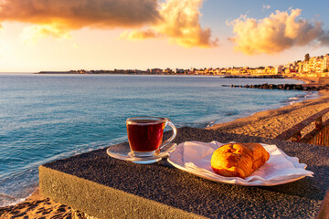 concept of street outdoor breakfast with a cup of tea or coffee on a morning coast during sunrise. landscape of city embarkment with sea water and cloudy sky on background
