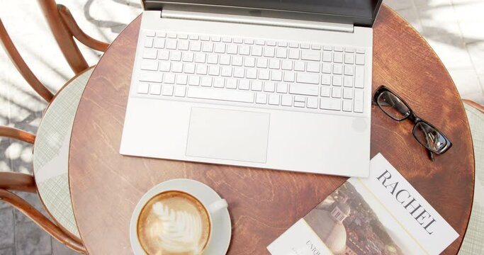 A laptop is open on a round table next to a cup of coffee and eyeglasses in a cafe
