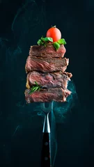 Fotobehang Slices of grilled meat barbecue steak Rib eye on meat fork on dark metal background close-up © Yaruniv-Studio