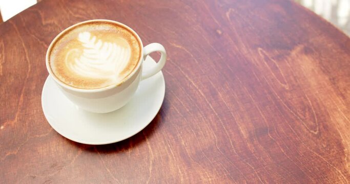 A cup of cappuccino with latte art sits on a wooden table in a cafe, with copy space