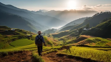 Fotobehang Rear view of a Male farmer strolling along rice terraces against the backdrop of high Mountains and the Sky at Sunset. Agriculture, Organic food concepts. © liliyabatyrova
