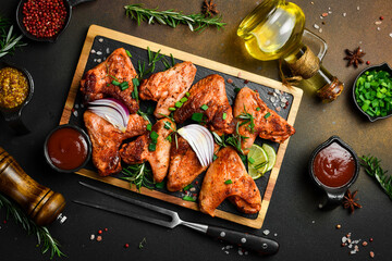 Fried chicken wings with onions and spices on a slate board. On a dark background.
