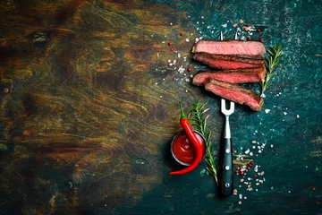 Fotobehang Slices of beef steak on a metal fork on a dark background. Top view. Free space for text. © Yaruniv-Studio