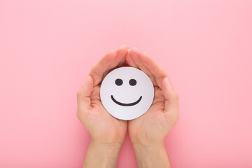 Young adult woman hand holding and showing happy smiling face on pastel pink table background....