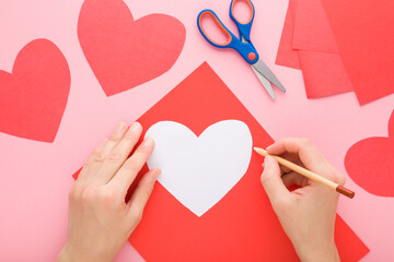 Young adult woman hand outlining contour with pencil for cutting red heart shape from application...