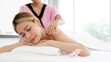 Obraz na płótnie Canvas Relaxing young Asian woman lying down and closing her eyes on massage beds while receiving a massage from a therapist at an Asian luxury spa salon and a wellness center, waiting for Spa salon concept