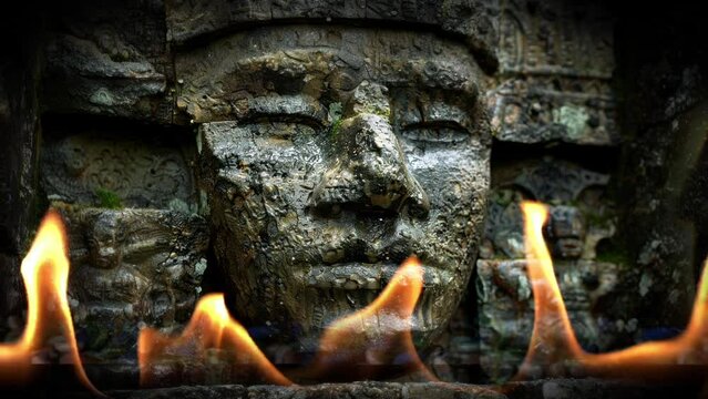 A slow zoom into an ancient face carving with flickering light and fire.	