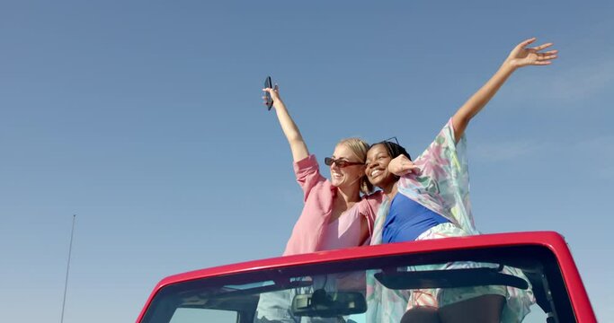 Young African American woman and Caucasian woman celebrate joyfully in a red car on a road trip