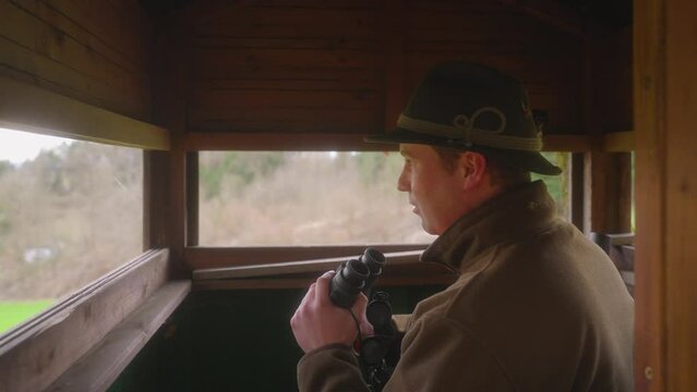 hunter looking through binoculars in high seat