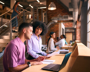 Male And Female Businesspeople Meeting In Office Discussing Documents With Colleagues In Background