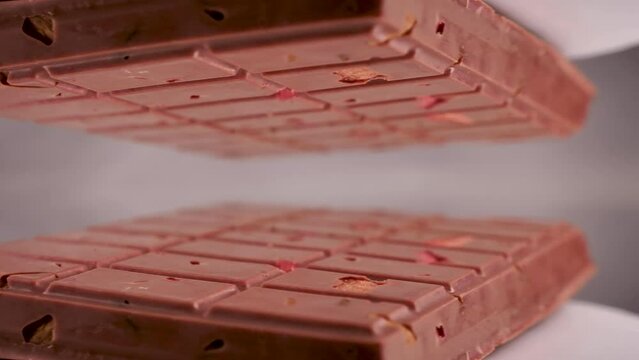 Close-up a milk ruby chocolate bar with chunks of nuts almonds and strawberry, displayed against a gray background is placed on a reflective surface, creating a mirrored image of itself