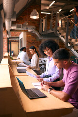 Male And Female Businesspeople Meeting In Office Discussing Documents With Colleagues In Background