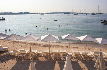 Rows of white umbrellas and sun loungers line the golden sandy beach in Cannes in the French Riviera in the early morning while a few swimmers and anglers have already started the day.