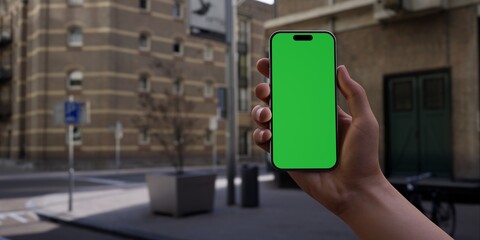 Hand holding a smartphone with a green screen on an urban city street background - 757299814