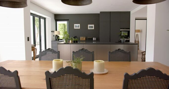 A modern kitchen with dark cabinetry is viewed from a wooden dining table