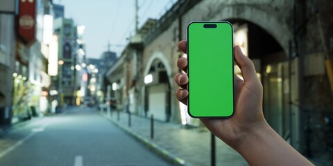 Man is holding a smartphone with a green screen against a urban nightscape - 757308205