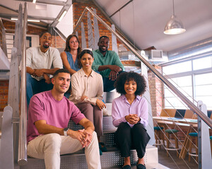 Portrait Of Smiling Multi-Cultural Business Team Sitting On Stairs In Modern Open Plan Office  - 757311276