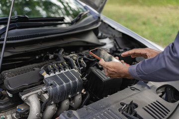 Auto mechanic looks under the hood of a broken car and checks the oil level on the side of the...