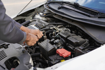 Auto mechanic looks under the hood of a broken car and checks the oil level on the side of the...