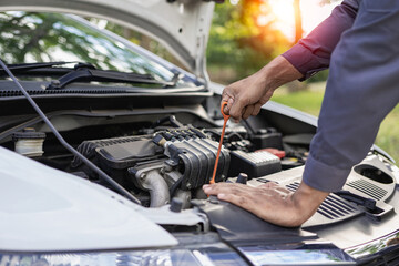 Auto mechanic looks under the hood of a broken car and checks the oil level on the side of the...