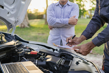 Auto mechanic looks under the hood of a broken car and checks the oil level on the side of the...