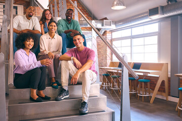 Portrait Of Smiling Multi-Cultural Business Team Sitting On Stairs In Modern Open Plan Office  - 757313015