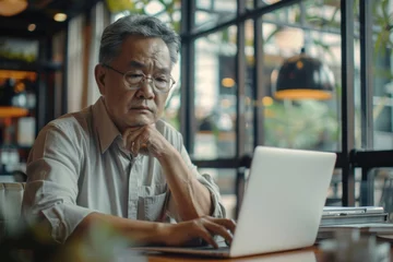 Fotobehang Serious and thoughtful businessman working inside office sitting at table using laptop at work, mature asian boss in shirt thinking and typing on keyboard. Generative AI © Moments Captured