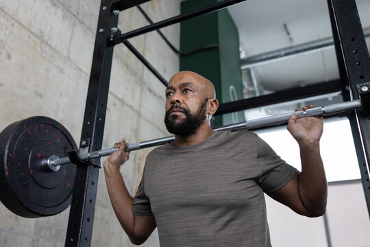 Mature African American male weight training with a barbell in a fitness gym