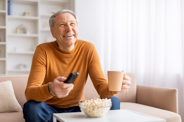 Happy senior man with remote control watching TV
