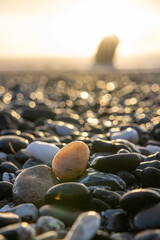 A small rock is sitting on a beach with a large rock in the background