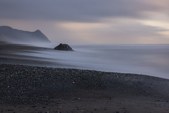 A rocky beach with a large rock in the foreground - Powered by Adobe