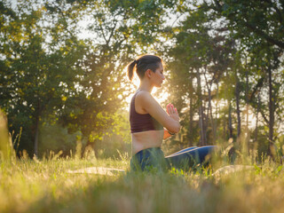 Young asian woman doing meditation in morning or evening at park, healthy woman relaxing and practicing yoga at city park. Mindfulness, destress, Healthy habits and balance concept