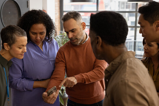 Group of colleagues in an office gathered around to look at smartphone