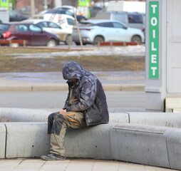 A homeless beggar sleeping sitting on a stone bench near a public toilet, Kollontai Street, St. Petersburg, Russia, March 13, 2024