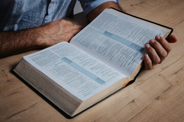 Man is reading the bible, holding with his hand the holy book, in a low-light environment