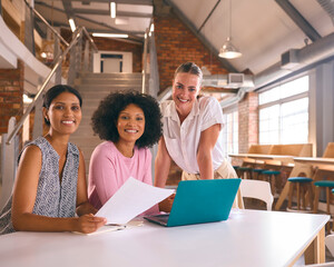 Portrait Of Young Businesswomen Meeting In Modern Office Sitting Around Table Working On Laptop Together