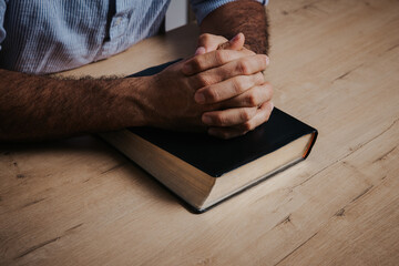 Man is praying with his hands together over the bible