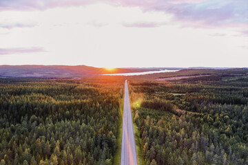 Sonnenuntergang über weitem Wald mit gerader Straße in Skandinavien Roadmap Drohne - obrazy, fototapety, plakaty