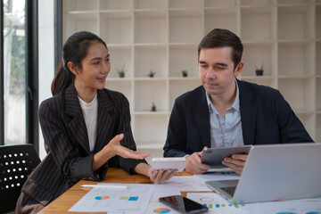 Two business people using a laptop ipad togerher in an office, a man and a women analyzing documents stat at office