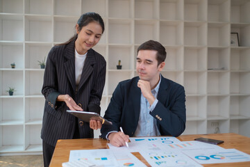 Two business people using a laptop ipad togerher in an office, a man and a women analyzing documents stat at office