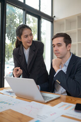 Fototapeta premium Two business people using a laptop ipad togerher in an office, a man and a women analyzing documents stat at office
