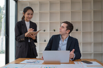 Two business people using a laptop ipad togerher in an office, a man and a women analyzing documents stat at office