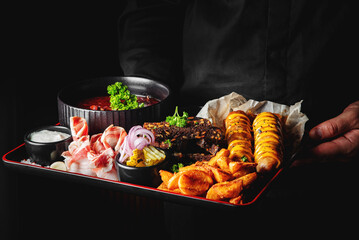 chef or waiter hold delectable platter of assorted appetizers, including grilled meat, soup, sausages, fries, and dips