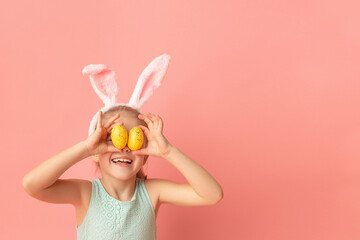 Portrait of cute smiling girl with Bunny ears and yellow Easter eggs, closes eyes with testicles,...