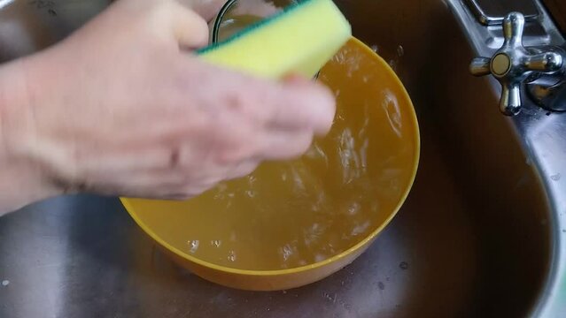 Unas manos de  mujer lavando un vaso de vidrio con una esponja, jab&oacute;n y agua  en un fregadero.