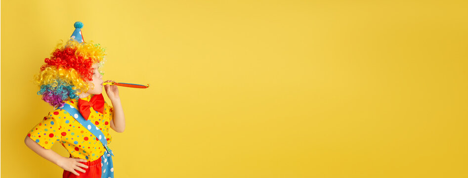 Banner. Funny kid clown against yellow background. Happy child playing with festive decor. Birthday and 1 April Fool's day concept