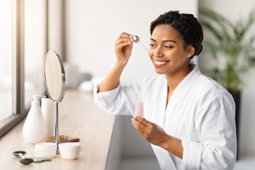 Smiling black woman using dropper to apply face serum from bottle