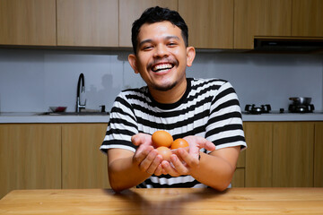 an asian man looks happy and shows chicken eggs in the kitchen