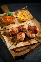 Close-up of chicken fillet wrapped in bacon on a wooden board with parchment