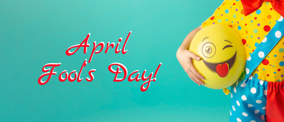 A bright yellow ball with a cheerful face in the hands of a clown child. Birthday and 1 April Fool's day concept